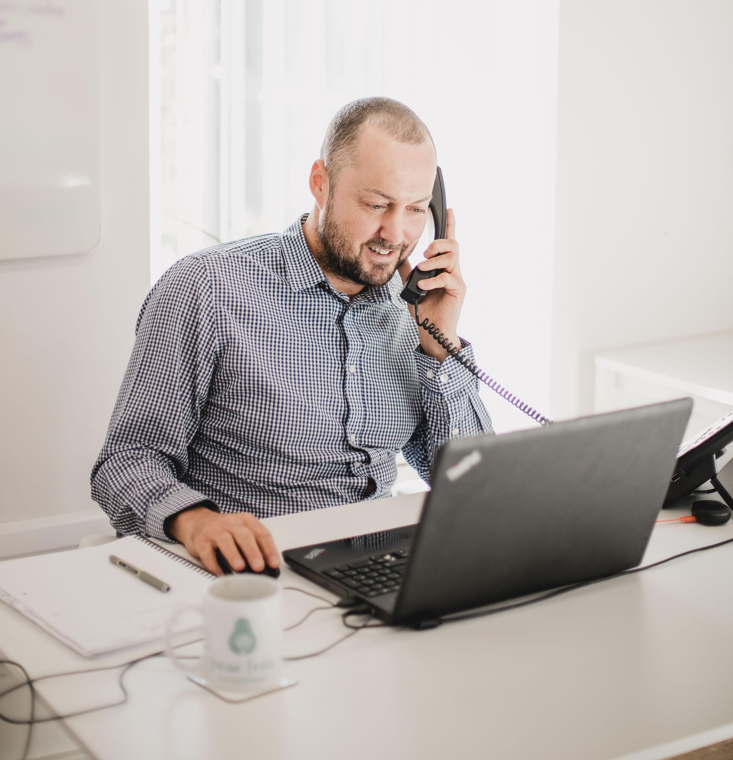 Photo of Glen at his desk, looking at his laptop and speaking on the phone