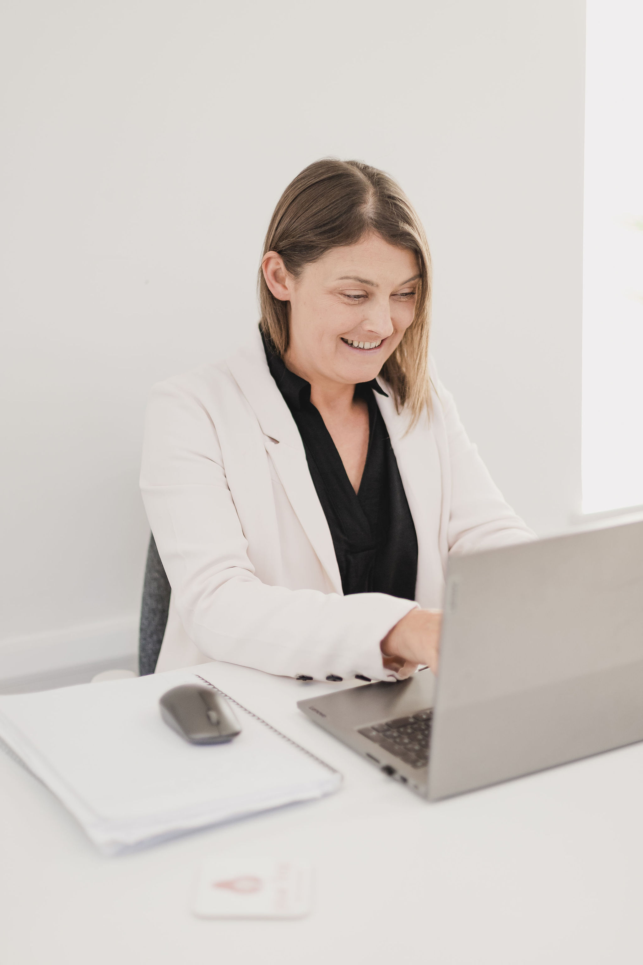 Photo of Jo sat at her desk, typing on her laptop, and smiling