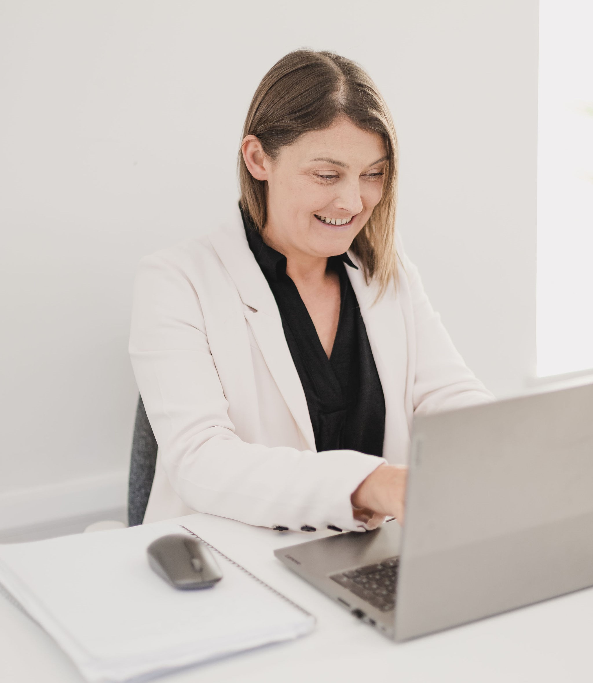 Photo of Jo sat at her desk, typing on her laptop, and smiling